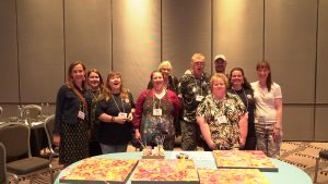 A group of people smile at the camera with paintings in front of them