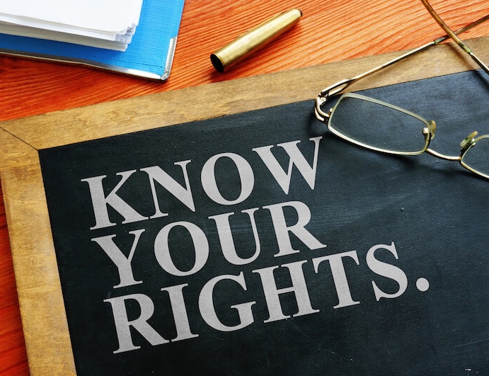 Corner of blackboard visible on a tabletop. The blackboard has a wooden frame and the words "Know your rights" on it. There are glasses resting on top and the corner of a binder is visible in the top left corner.