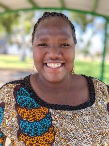 Photo of Esther smiling at the camera. She has her hair pulled back and is wearing a printed top.