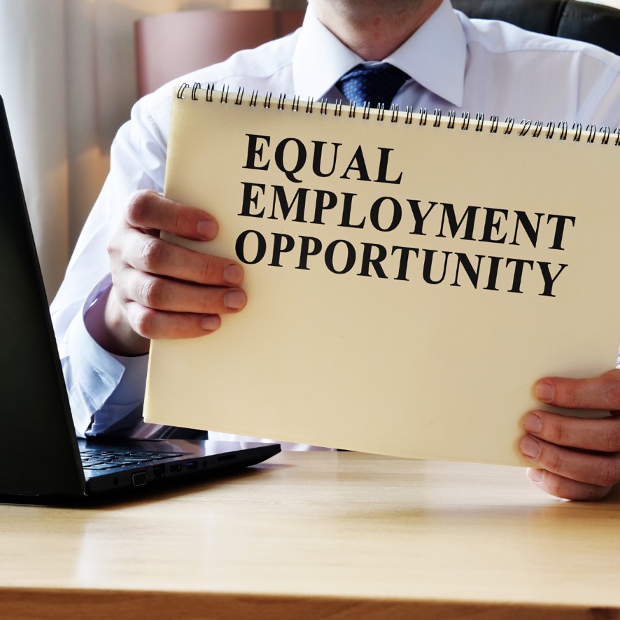 Photo of man wearing shirt and tie holding a sign in front of him with the text "Equal Employment Opportunity".