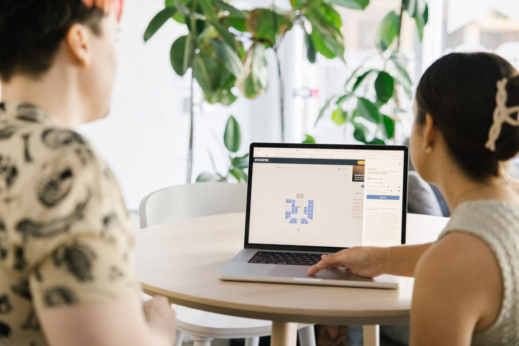 Two people are facing a laptop computer and looking at the screen.