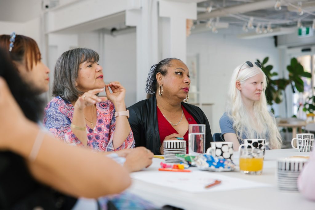 A group of people are sitting at a table - looking towards a presenter at the front of the room.