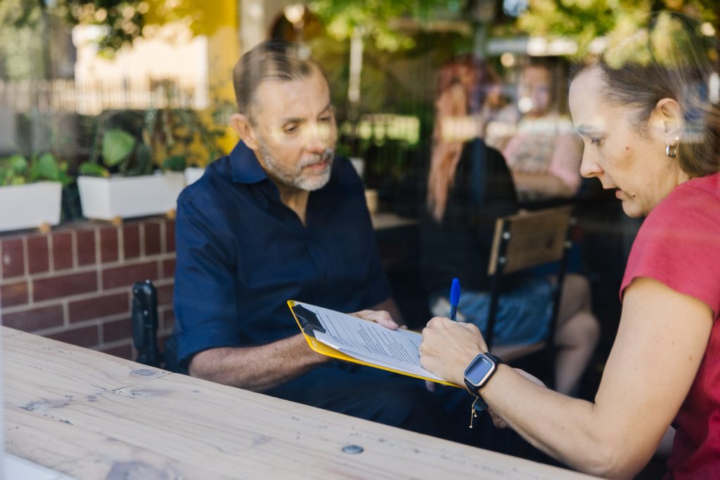 A man with a blue long sleeve shirt is holding a clipboard with paper